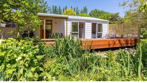 Une maison mobile de plain-pied dotée d’une terrasse en bois, entourée d’une végétation luxuriante et d’arbres.