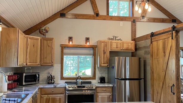 A kitchen with wooden cabinets, a stainless steel refrigerator, a stove, and a large island with stools.