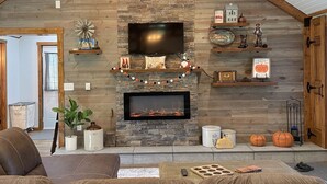 A cozy living room with a stone fireplace, wooden beams, and a flat-screen TV.