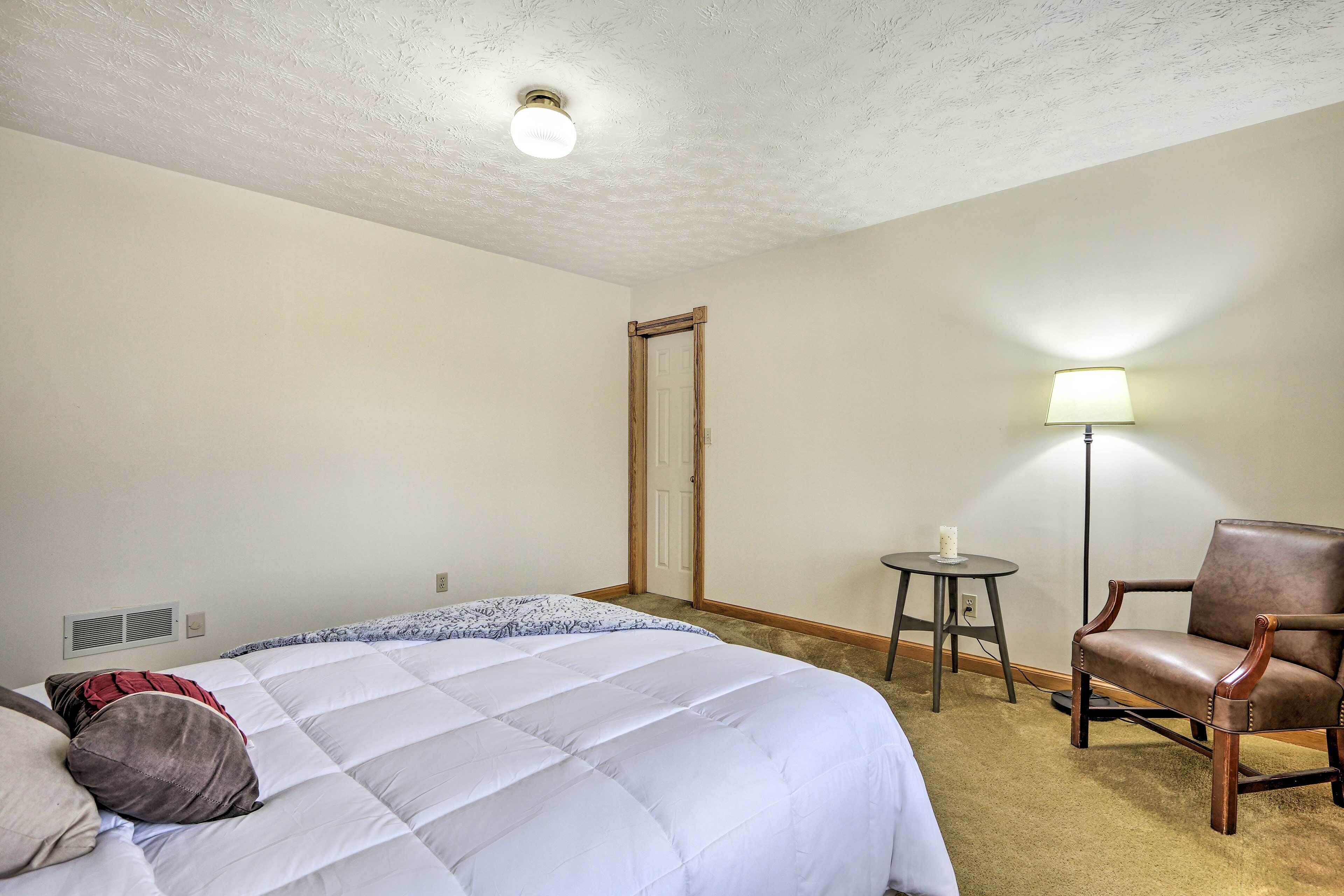Una habitación de hotel con una cama, una silla, una lámpara y una mesita.