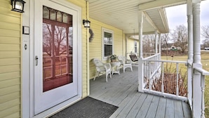 A porch with a white door, two wicker chairs, a small table, and a potted plant.