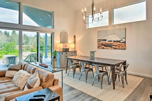 A modern living room with a large dining table, a sofa, and a view of the outdoors. - Modern Ocean Shores Getaway with Dock! (Ocean Shores)