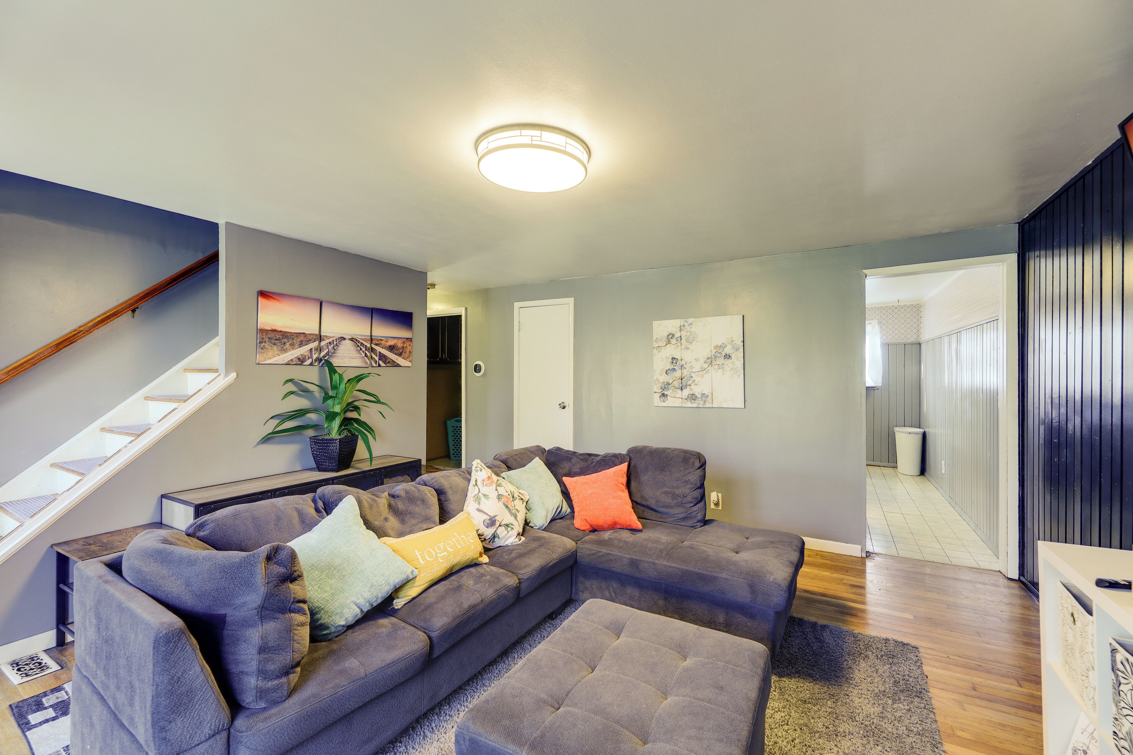Een moderne woonkamer met een hoekbank, een trap en een gang naar een andere kamer.