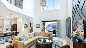 A spacious living area with a large L-shaped sofa, a coffee table, and a television on a wooden cabinet.