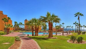 A resort with a central pool, palm trees, and a clear blue sky.