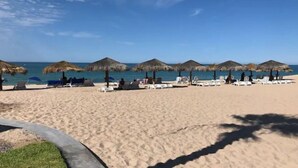 A beach with sun loungers and thatched umbrellas, a clear sky, and a calm sea.