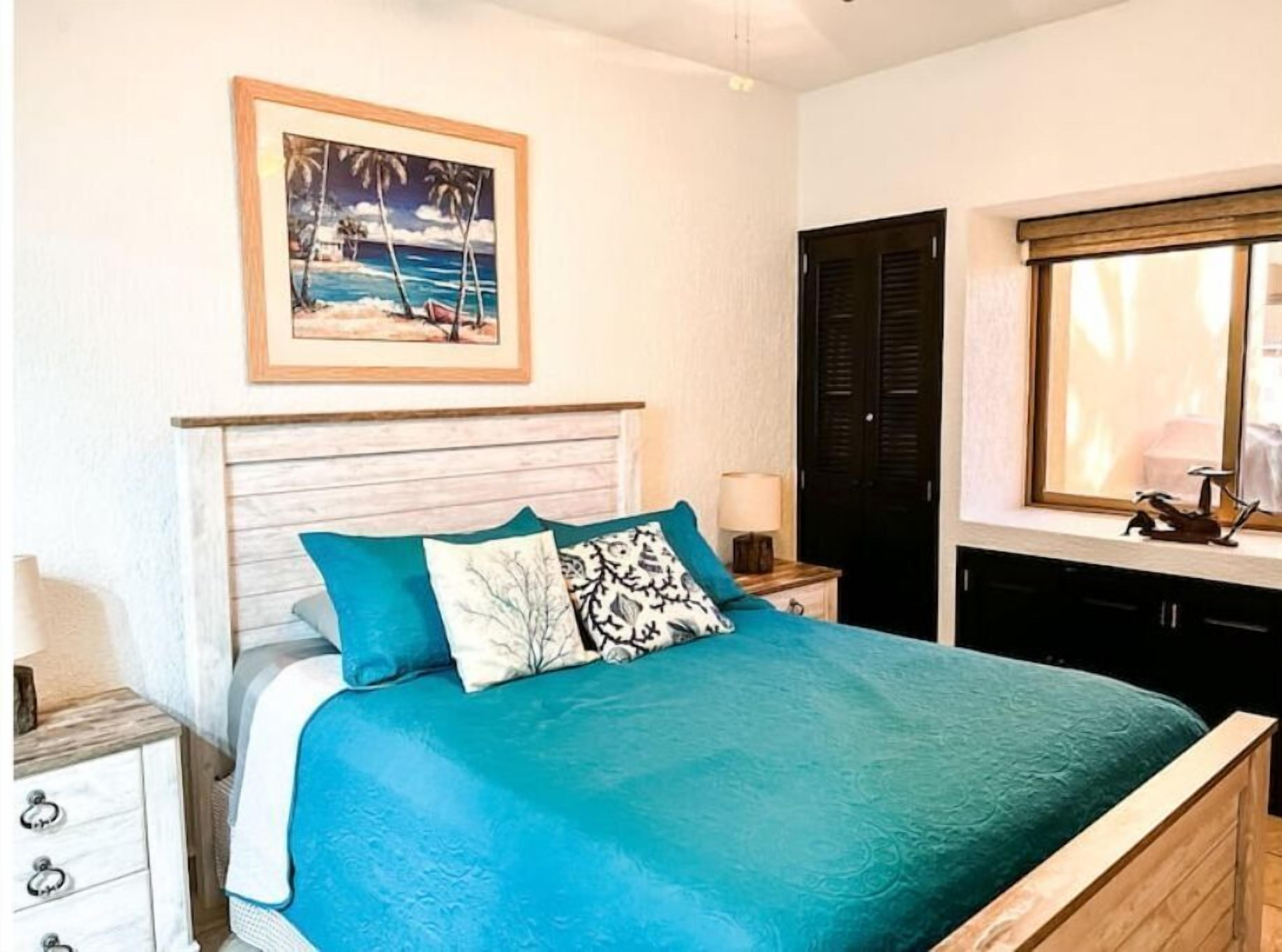Un dormitorio con cama, mesita de noche, lámpara, ventana con persianas y un cuadro en la pared.