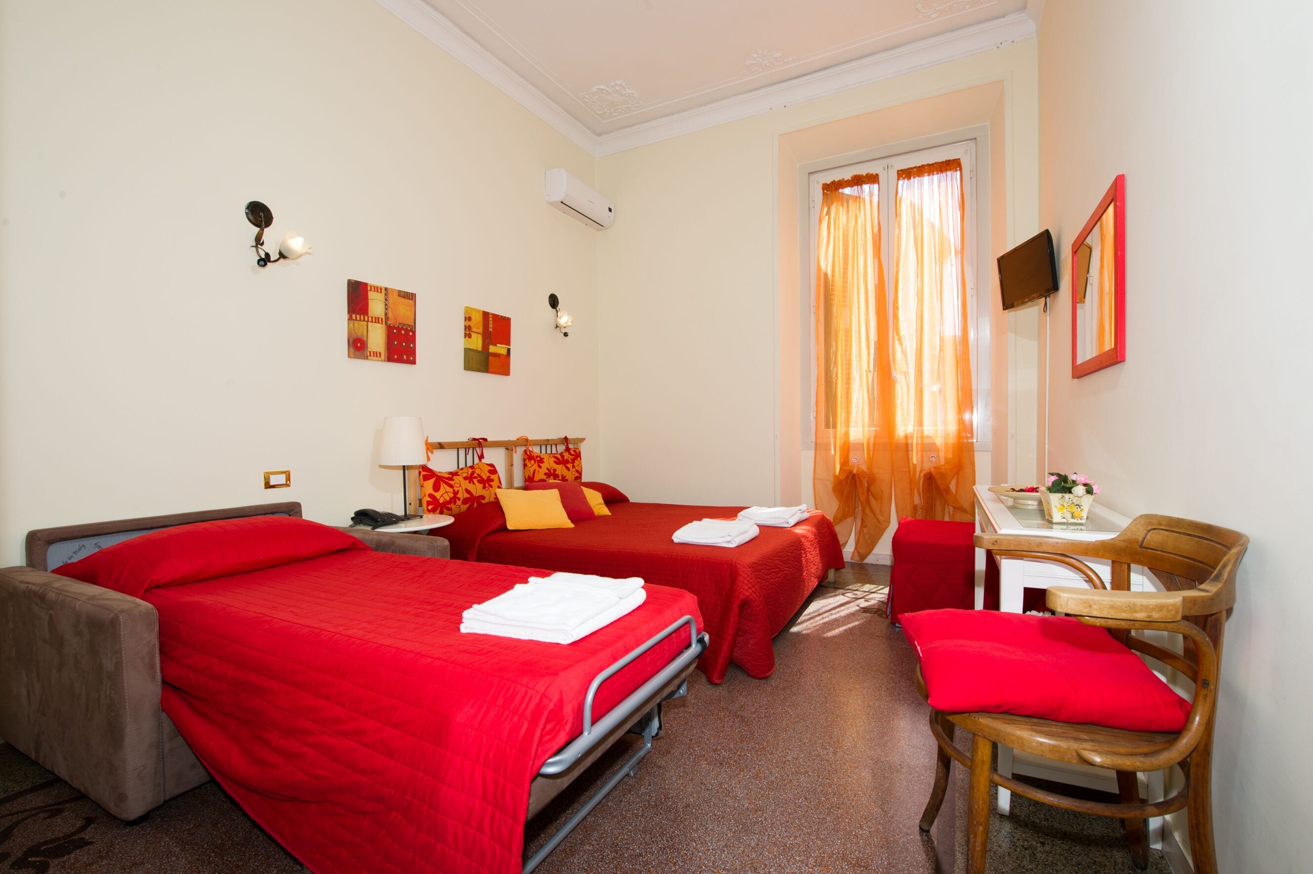 Ein Hotelzimmer mit zwei Einzelbetten, einem Schreibtisch mit Stuhl, einem kleinen Tisch mit Vase und einem Spiegel an der Wand.