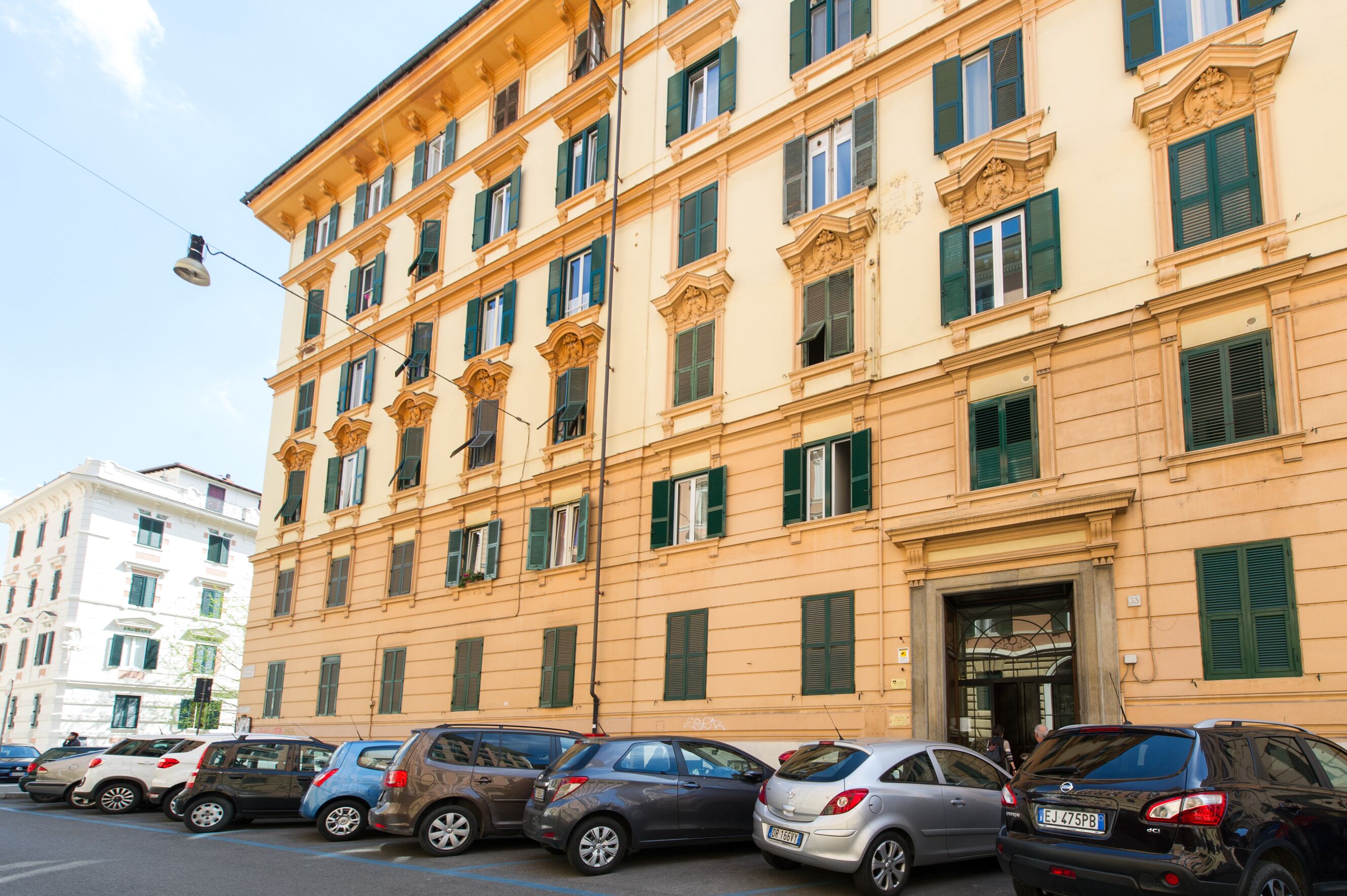 A multi-story building with a classic architectural style, featuring a central entrance with a decorative archway and multiple windows with green shutters.