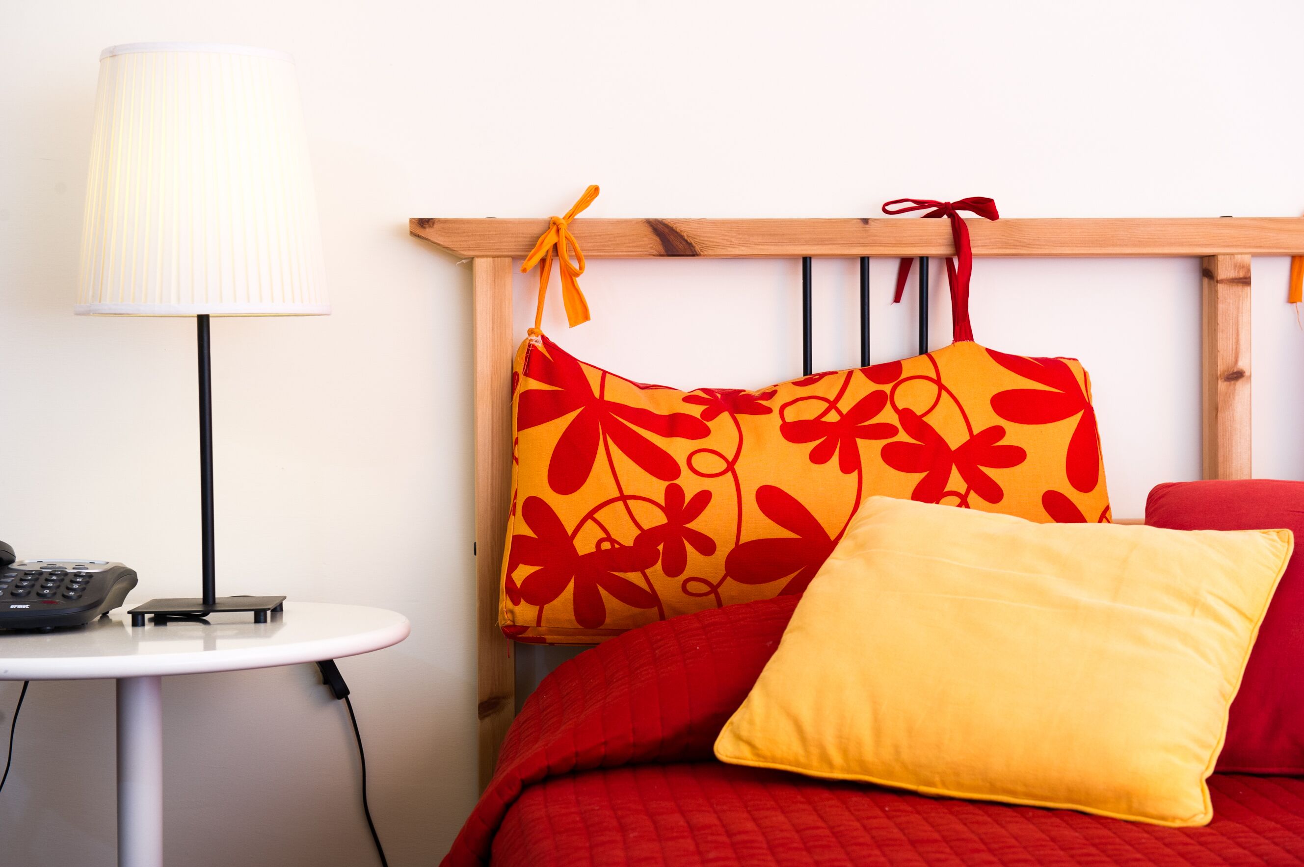 Een bed met rode beddengoed, een geel kussen en een kussen met een rood-geel bloemenmotief.