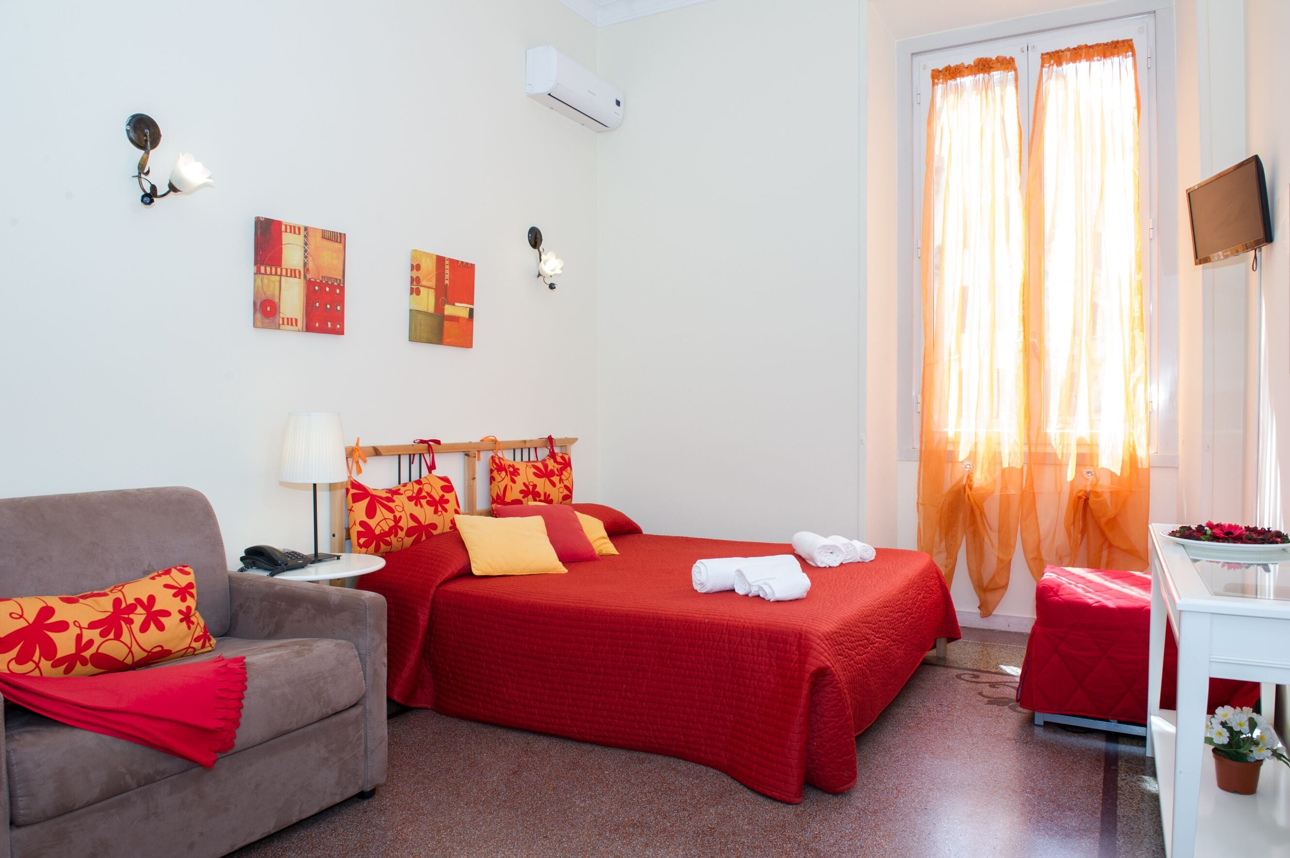 A hotel room with a bed, a sofa, a TV, and a window with curtains.