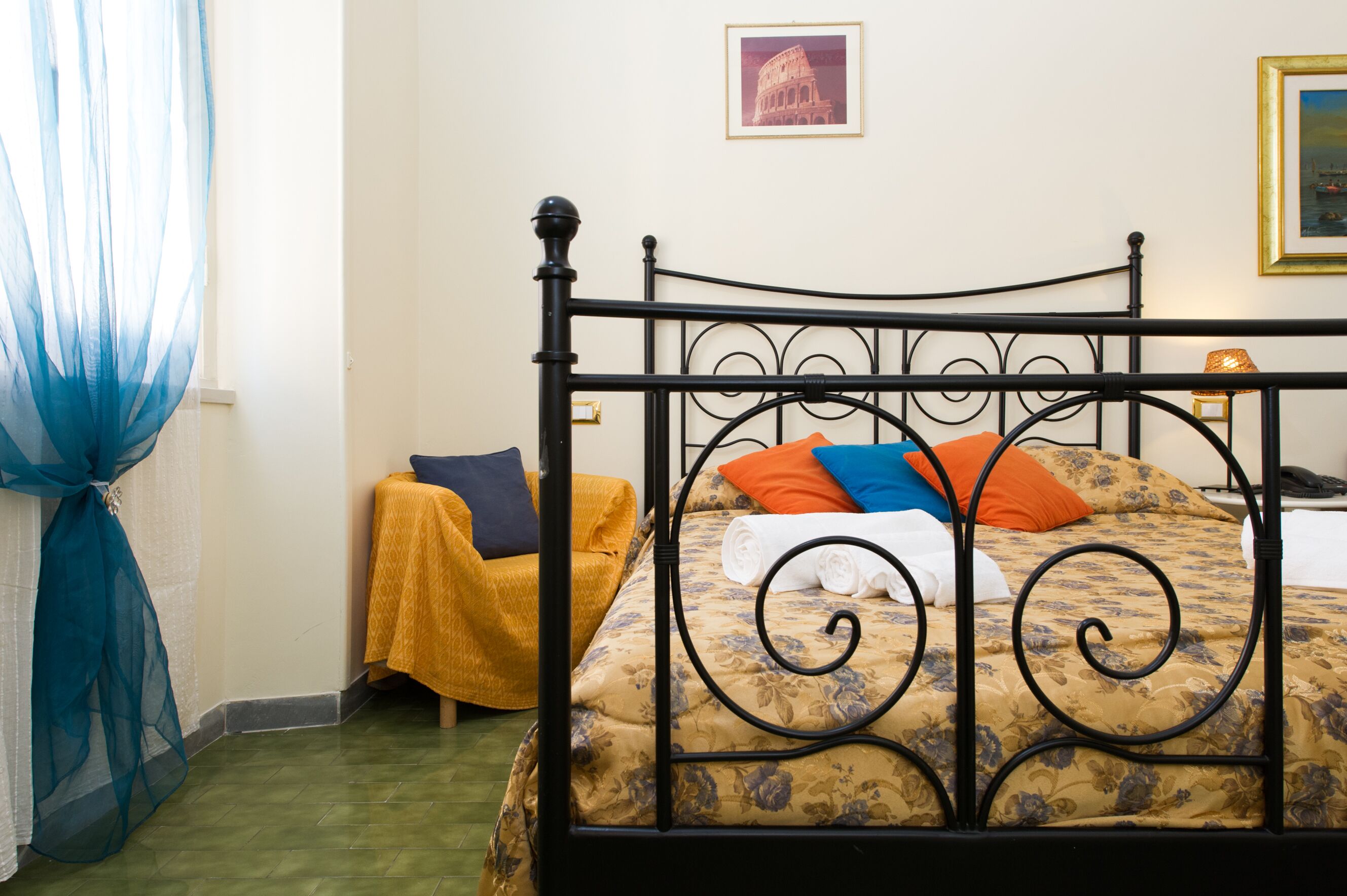 Una cama con una colcha estampada, una silla amarilla y una cortina azul.