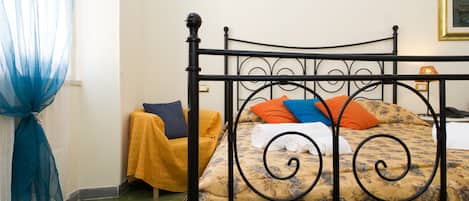 Una cama con una colcha estampada, una silla amarilla y una cortina azul.
