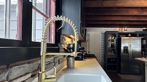 A kitchen with a white sink, a gold faucet, and a stone wall.
