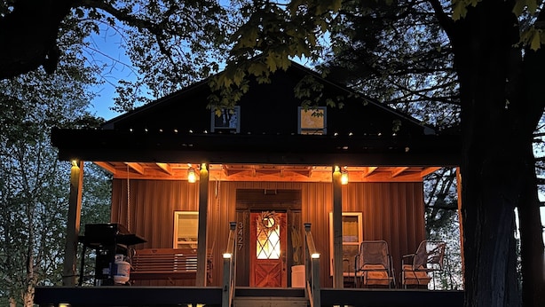 A rustic cabin with a wooden exterior, a stone foundation, and a porch with outdoor seating.