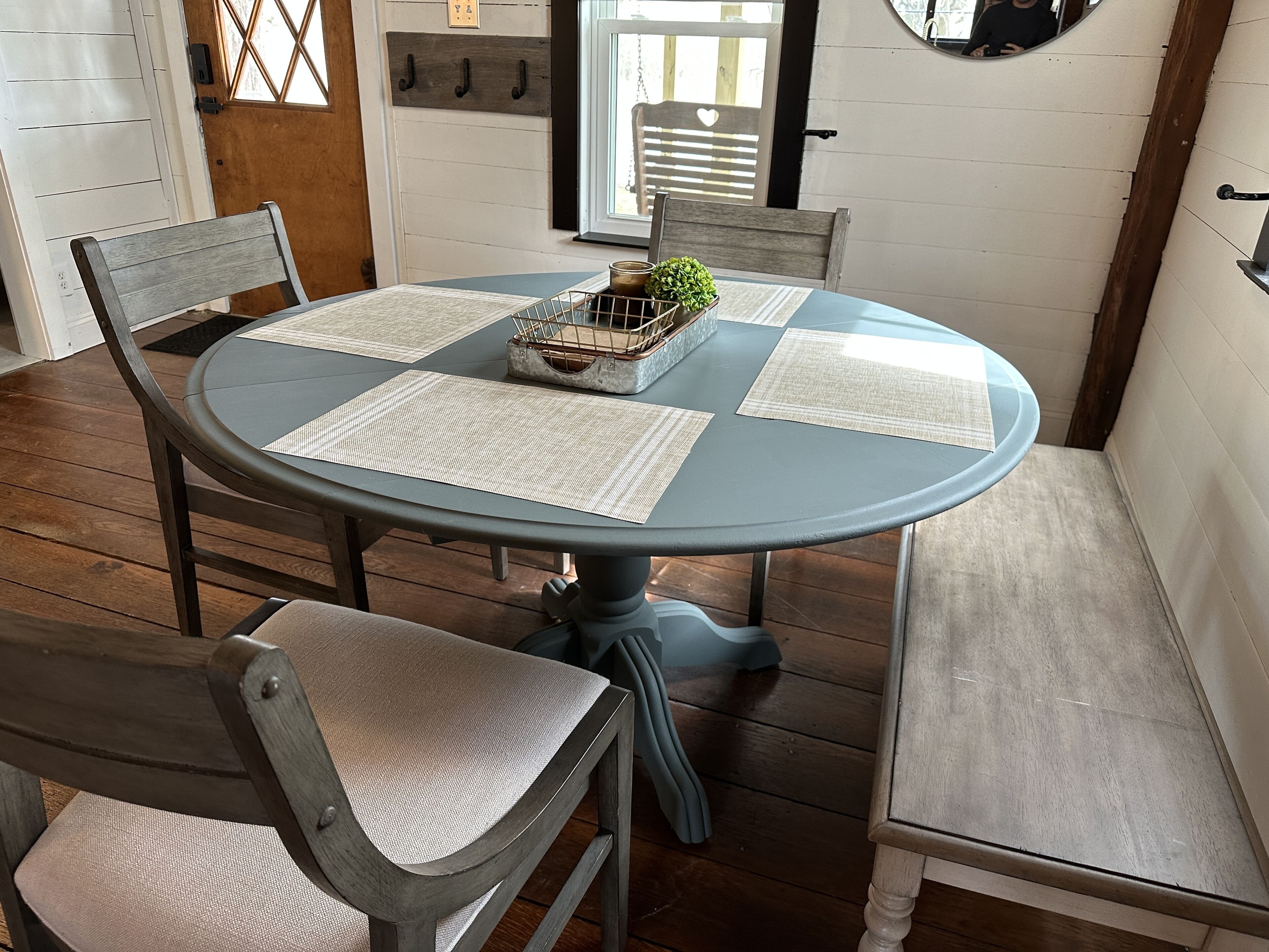 Een ronde eettafel met vier stoelen, elk met een geweven placemat. De tafel is gedekt voor vier personen.