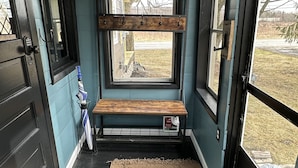 A narrow hallway with a bench, a small table, and a window with a view of the outdoors.