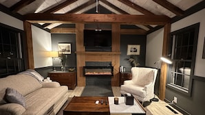 A cozy living room with a fireplace, wooden beams, a sofa, a chair, and a coffee table.