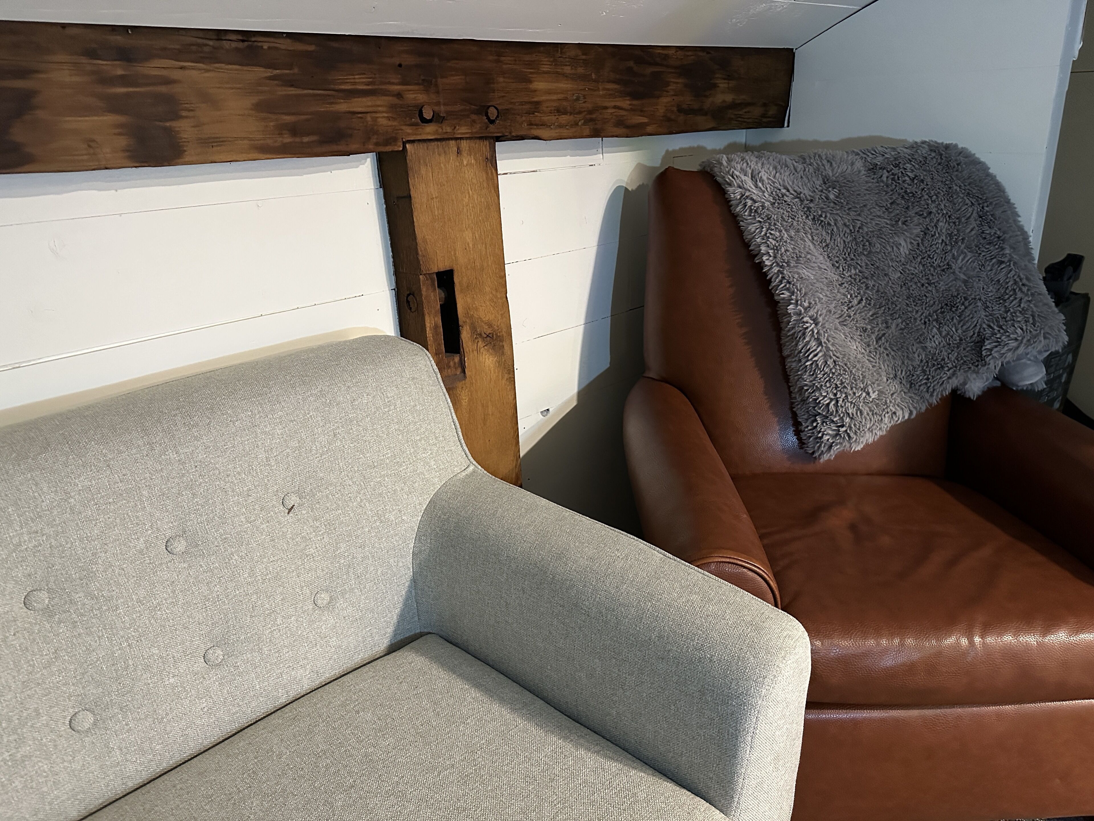 A room with a light grey sofa and a brown leather chair, both with a wooden headboard.
