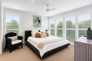 Ein Schlafzimmer mit Bett, einem Sessel, einem Deckenventilator und einem Gemälde an der Wand.