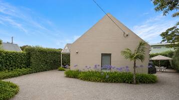 A single-story building with a triangular roof, surrounded by a gravel driveway, a well-maintained hedge, and flowering plants.