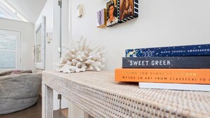 Un salon moderne avec une table en osier sur laquelle sont posés des livres, un mur blanc orné de tableaux encadrés et un fauteuil en forme de poire de couleur grise.
