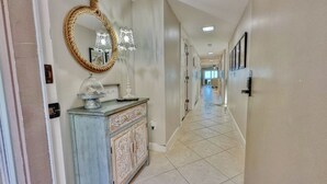 A hallway with a decorative console table, a mirror, and a chandelier. - Beachfront Paradise, Retro Twist, Exquisite Views, Private Entrance, EV Car Charger!   (Indian Shores)