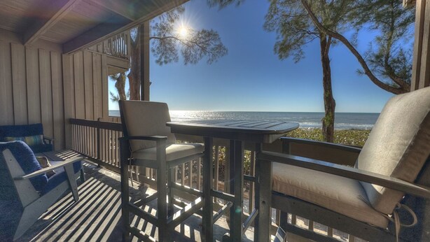 A covered outdoor seating area with a table and chairs, overlooking a beach. - Beachfront Paradise, Retro Twist, Exquisite Views, Private Entrance, EV Car Charger!   (Indian Shores)