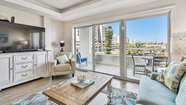 A spacious living room with a flat-screen TV, a sofa, a coffee table, and a balcony with a view of the city. - Stunning & Spacious Waterfront, French Country Coastal Style, Complex Pool & Hot Tub!   (Clearwater)