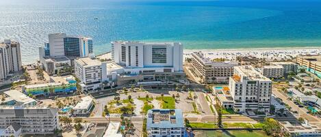 An aerial view of a coastal city with modern buildings, a marina, and a beach.