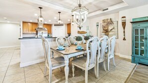 A dining area with a central island, white chairs, and a chandelier. - Stunning & Spacious Waterfront, French Country Coastal Style, Complex Pool & Hot Tub!   (Clearwater)