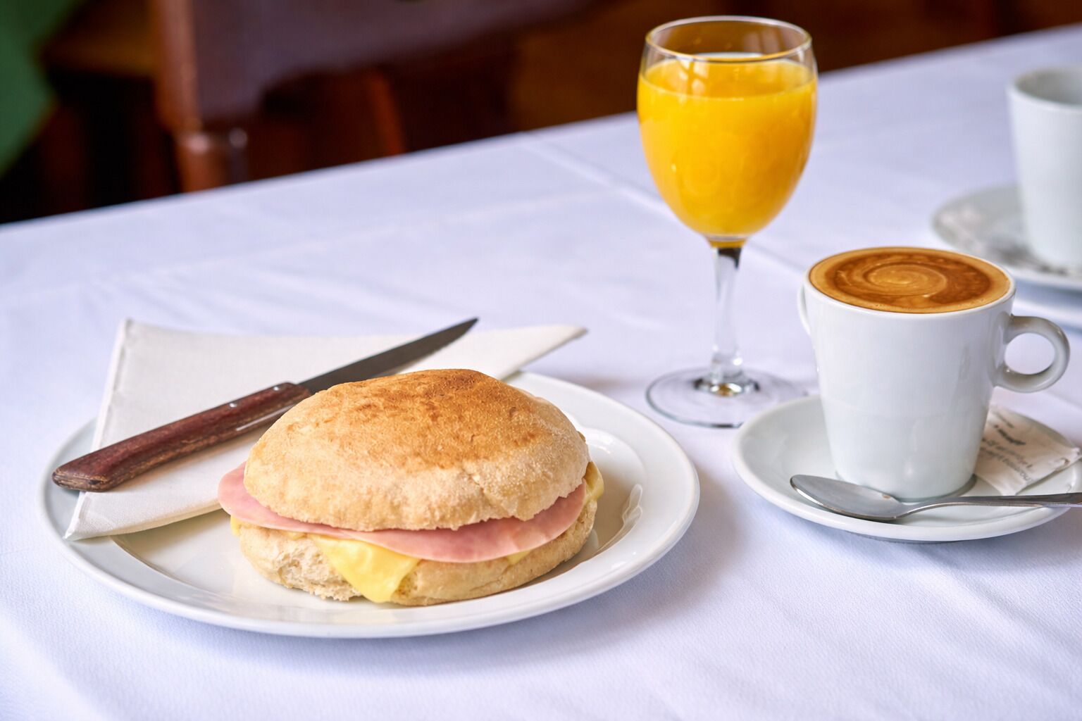 En morgenmadsopstilling med en sandwich, et glas appelsinjuice og en kop kaffe på et bord.