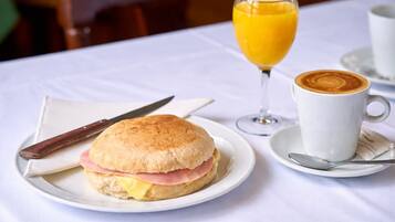 En morgenmadsopstilling med en sandwich, et glas appelsinjuice og en kop kaffe på et bord.