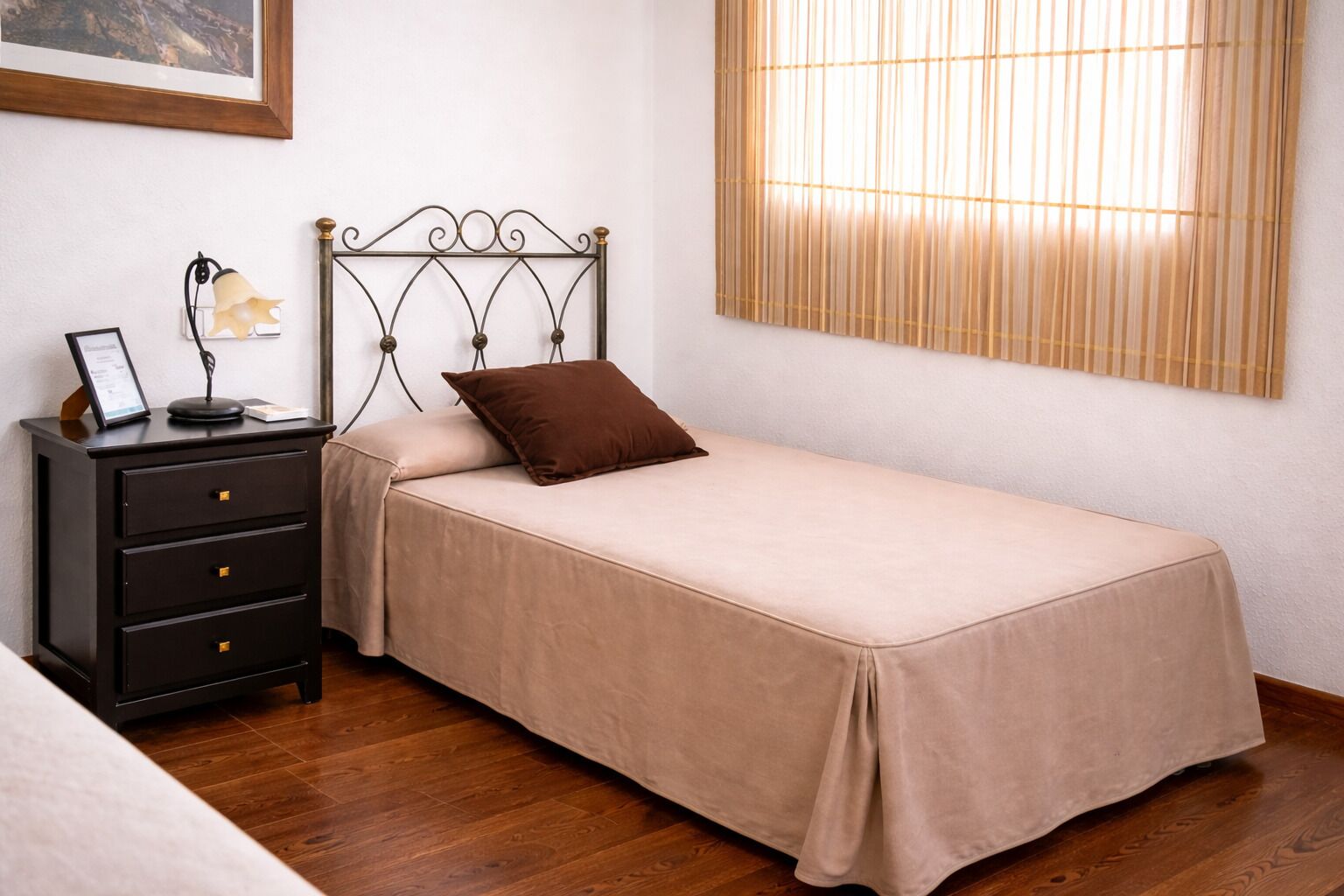 A bedroom with a single bed, a nightstand, a lamp, and a framed picture on the wall.