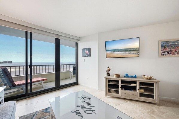 A living room with a glass door leading to a balcony with a view of the beach.