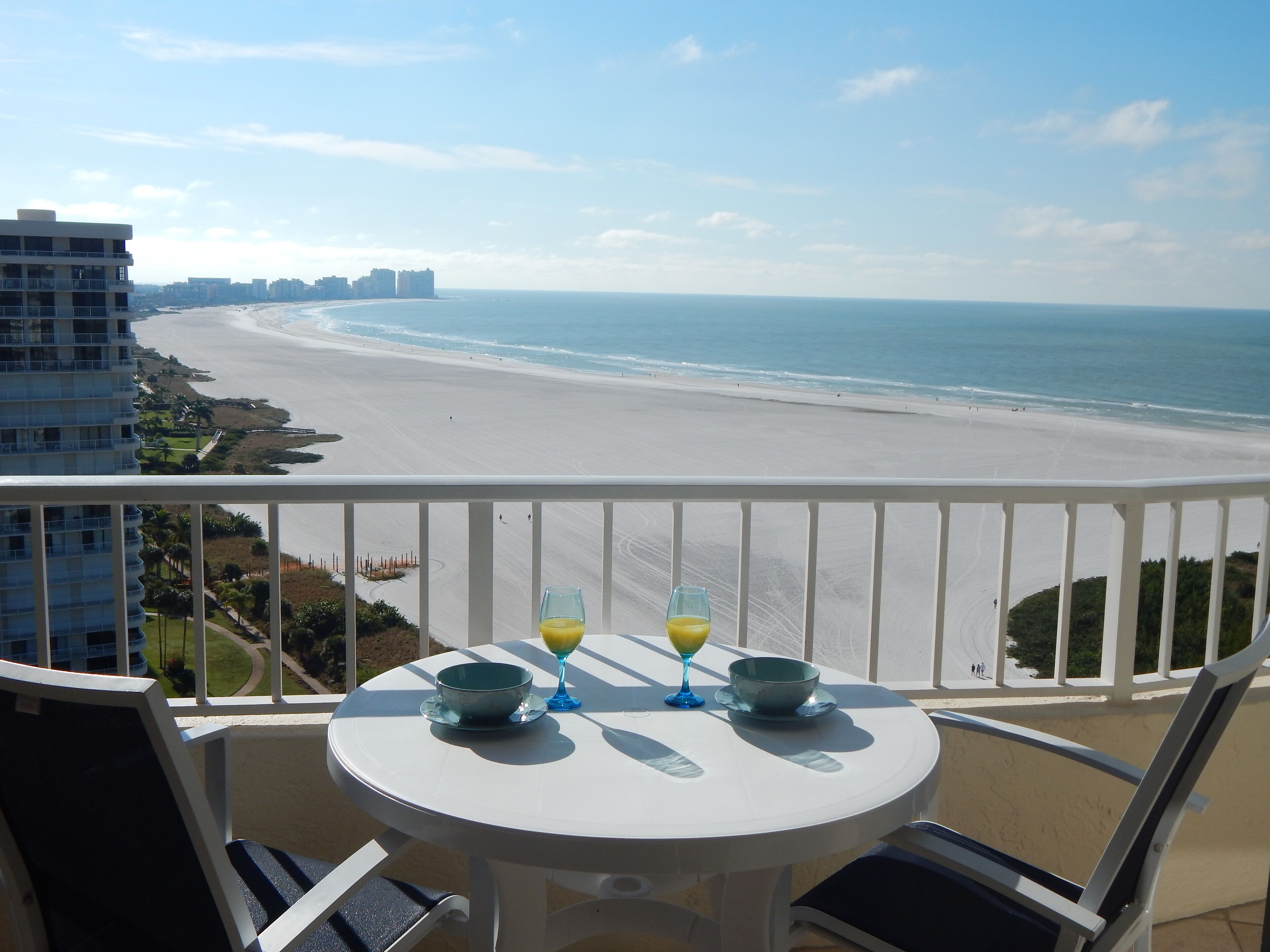 Ein Balkon mit Tisch, zwei Orangensaftgläsern und einer Schale. Blick auf Strand und Meer.