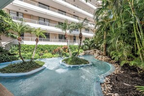 A hotel courtyard with a water feature, palm trees, and a multi-story building.