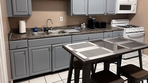 Une cuisine avec des meubles gris, un plan de travail en granit, un micro-ondes blanc, une cuisinière et un évier.