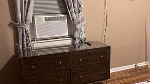 Une chambre à coucher avec une commode en bois, un téléviseur à écran plat fixé au mur et un lit avec une literie à motifs floraux.