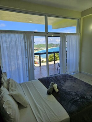 Een slaapkamer met een bed, uitzicht op een strand en een terras.