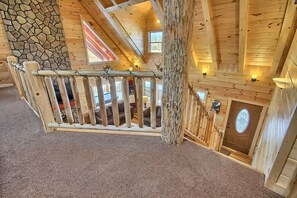 A wooden interior with a stone wall, a wooden staircase, and a view of a room with a fireplace. - Lone Star Lodge - Gorgeous Lodge in Hocking Hills (Logan)