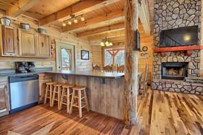 A rustic cabin interior with a stone fireplace, wooden bar stools, and a kitchen area with a dishwasher. - Lone Star Lodge - Gorgeous Lodge in Hocking Hills (Logan)