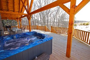 A wooden deck with a hot tub, outdoor furniture, and a view of a snowy landscape.