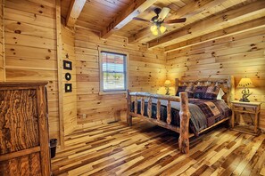 A wooden cabin bedroom with a bed, a ceiling fan, and a window.