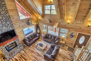 Amplia sala de estar con chimenea de piedra, piso de madera y sofás de cuero marrón.