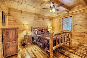 Un dormitorio de cabaña de madera con cama, mesitas de noche y ventilador de techo.