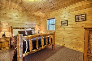 A wooden cabin bedroom with a bed, nightstands, a window, and wall-mounted pictures. - Lone Star Lodge - Gorgeous Lodge in Hocking Hills (Logan)