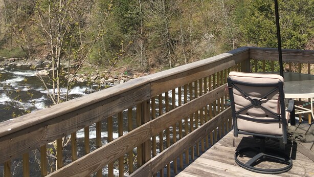 Una terraza de madera con una mesa y sillas, con vista a un río y una zona boscosa.