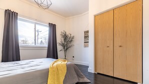 Une chambre à coucher avec un lit, des rideaux foncés, une fenêtre, une plante en pot et une armoire en bois.