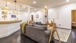 Un salon moderne avec un canapé gris, un plancher en bois et des luminaires suspendus.